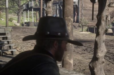 Eine Person sitzt in Red Dead Redemption 2 auf einer Bank in Valentine und schaut dem Treiben auf der Straße zu.