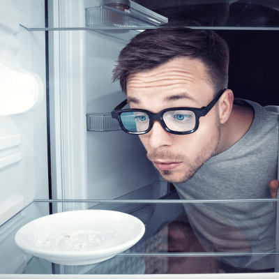Student guckt in einen leeren Kühlschrank - Er braucht Rezepte für Studenten