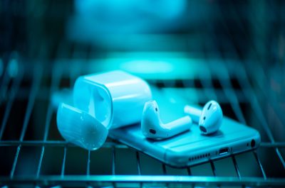Smartphone und kabellose Kopfhörer, die auf einem Gitter liegen und mit UVC-Licht bestrahlt werden.