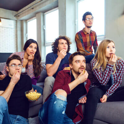 Eine Gruppe von Freunden verfolgt gespannt zusammen einen Film und essen Popcorn.