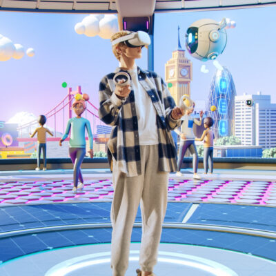 Ein Mensch trägt eine Virtual-Reality-Brille und Controller in den Händen. Er steht in einer futuristischen virtuellen Umgebung, die von Avataren bevölkert ist. Im Hintergrund sind stilisierte Gebäude und Wahrzeichen wie der Big Ben und eine moderne Skyline zu sehen. Die Umgebung wirkt bunt und dynamisch, mit verschiedenen Personen, die miteinander interagieren.