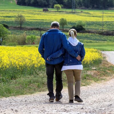 Paar läuft Arm in Arm über Feldweg mit Blumen im Hintergrund